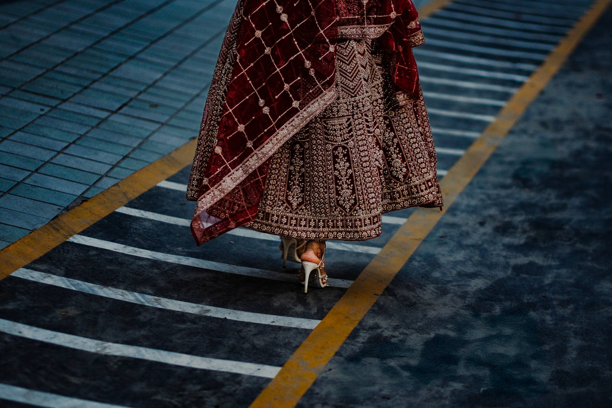 Bride's embroidered lehenga train and heels crossing a marked driveway